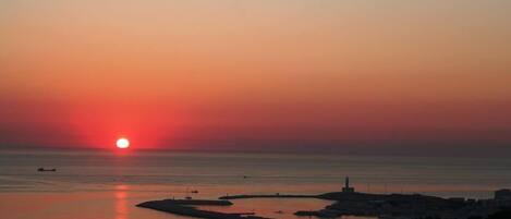 A sunset over a coastal area with a lighthouse and marina.