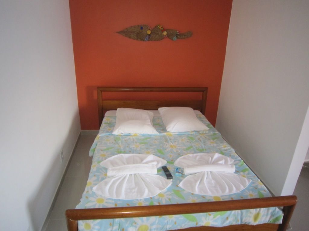 Uma cama de solteiro com colcha florida, duas almofadas brancas e cabeceira de madeira.