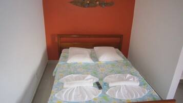 Uma cama de solteiro com colcha florida, duas almofadas brancas e cabeceira de madeira.