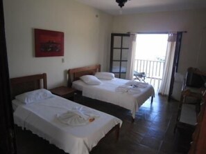 Habitación de hotel con dos camas individuales, cabecera de madera, una mesita y una silla.