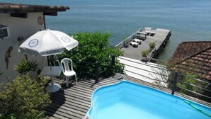 A pool area with a view of the sea, a deck with lounge chairs, and a patio with a table and chairs. - Pousada Pier 7400 (Angra dos Reis)