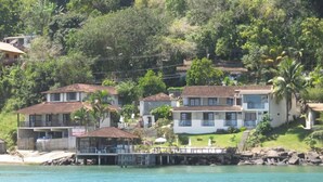 A coastal area with houses near the water, featuring a dock and a small boat. - Pousada Pier 7400 (Angra dos Reis)
