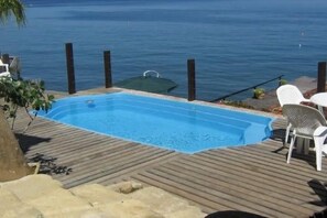 Piscina rectangular con cubierta de madera, rodeada por una cerca y con vistas a una masa de agua.