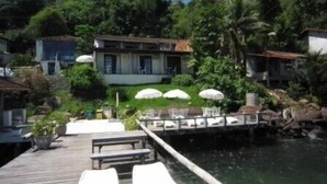 A wooden dock with lounge chairs and umbrellas overlooking a body of water, surrounded by lush greenery and buildings. - Pousada Pier 7400 (Angra dos Reis)