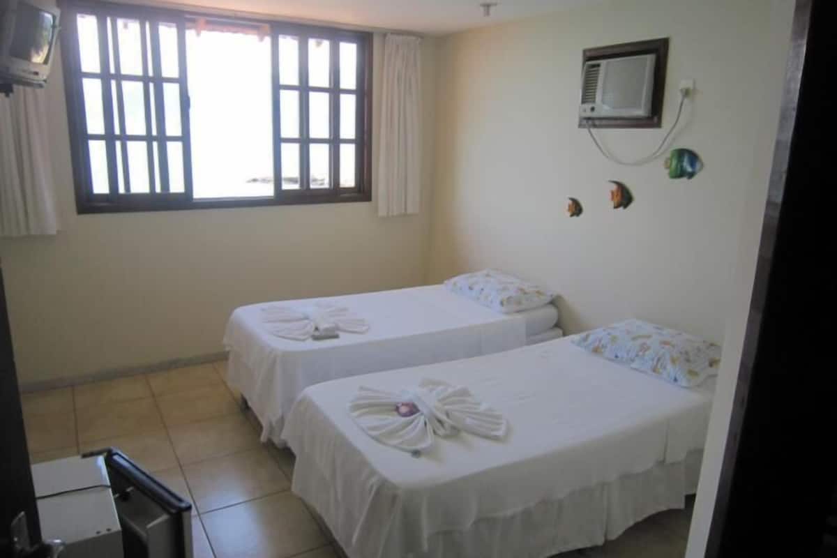 A hotel room with two beds, a window with curtains, a wall-mounted air conditioner, and a small TV.