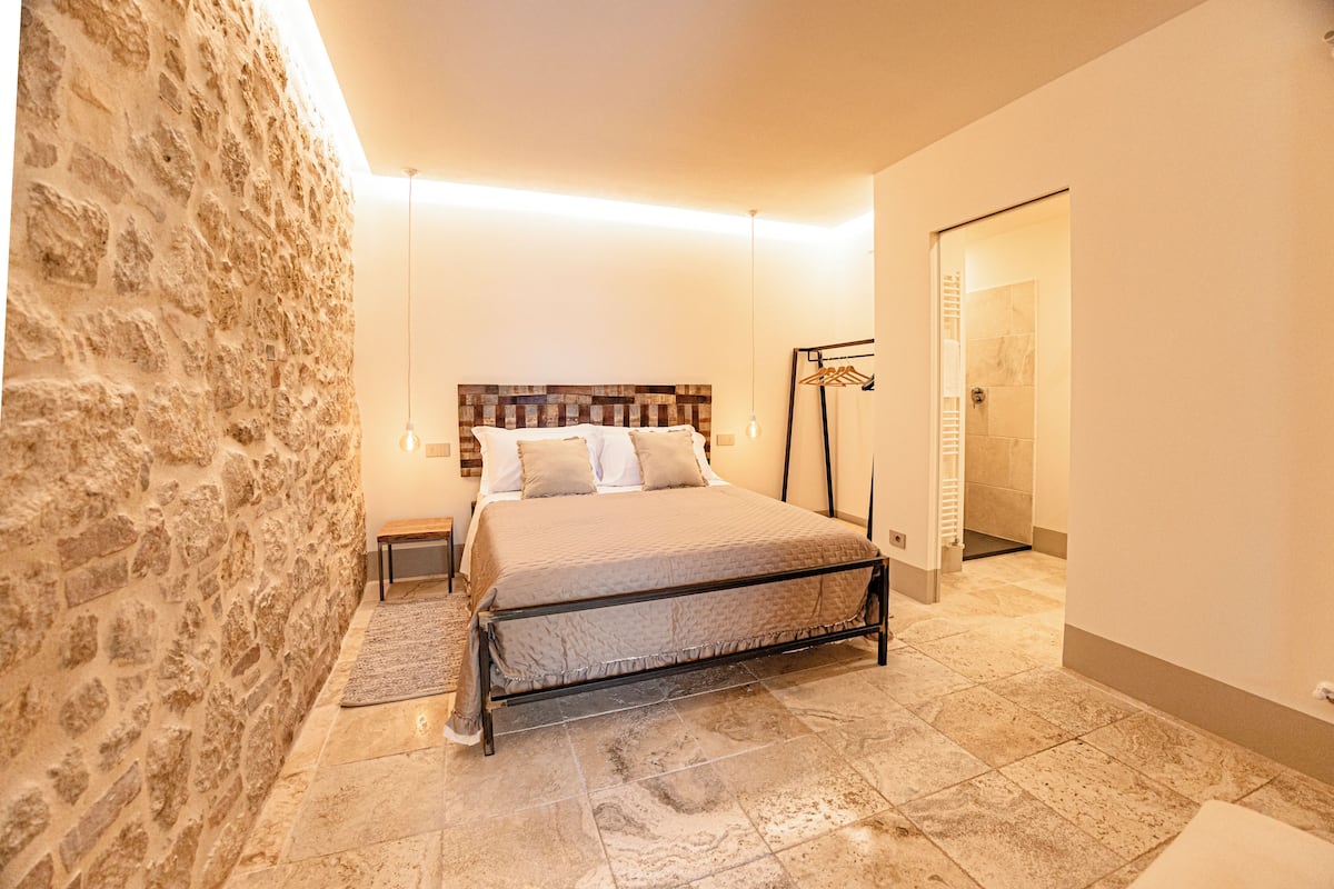 Een slaapkamer met een stenen muur, een bed met metalen frame, een nachtkastje en een hanglamp.