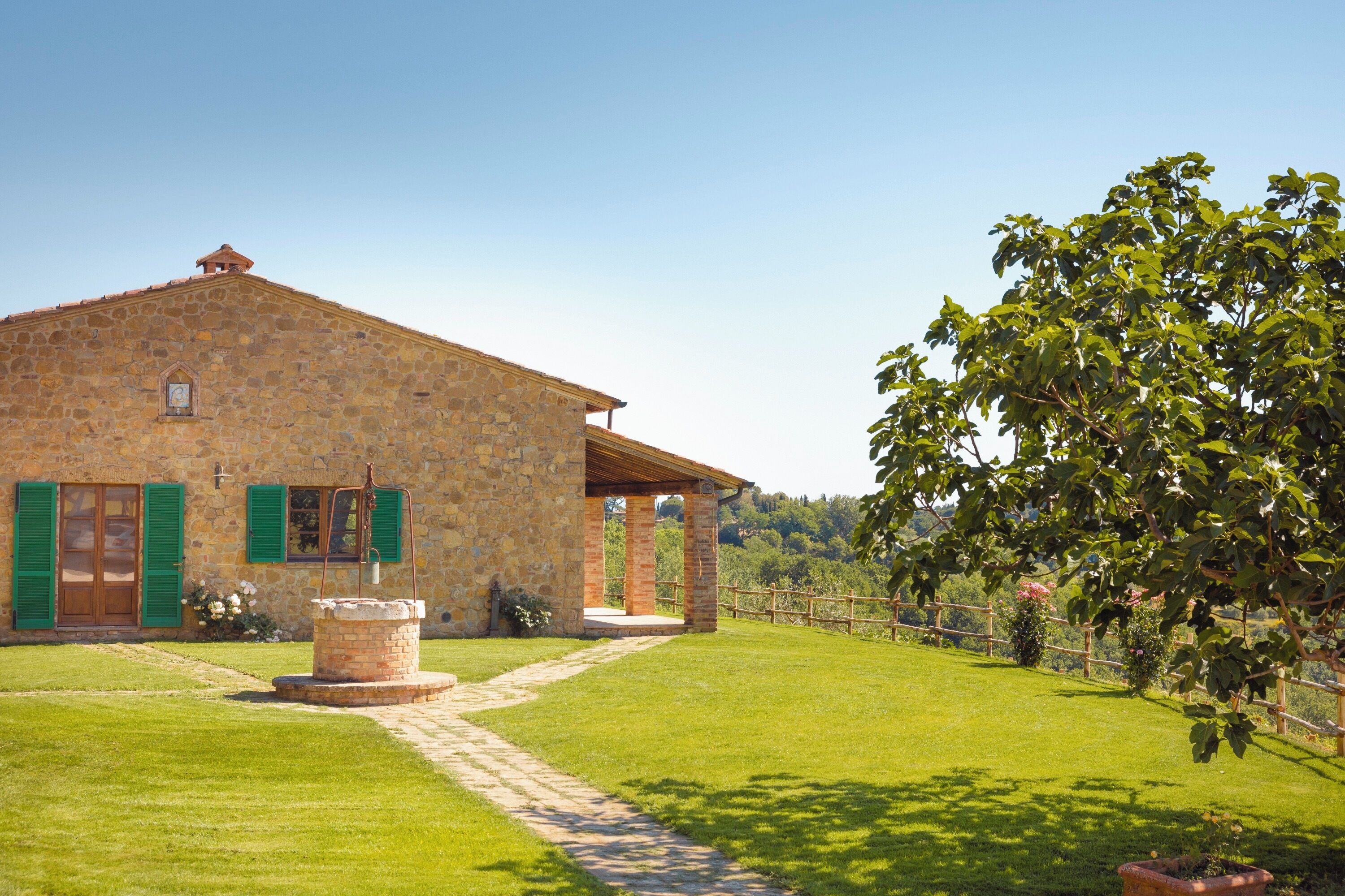 A stone building with a covered porch, a stone well, and a paved path leading to the entrance.