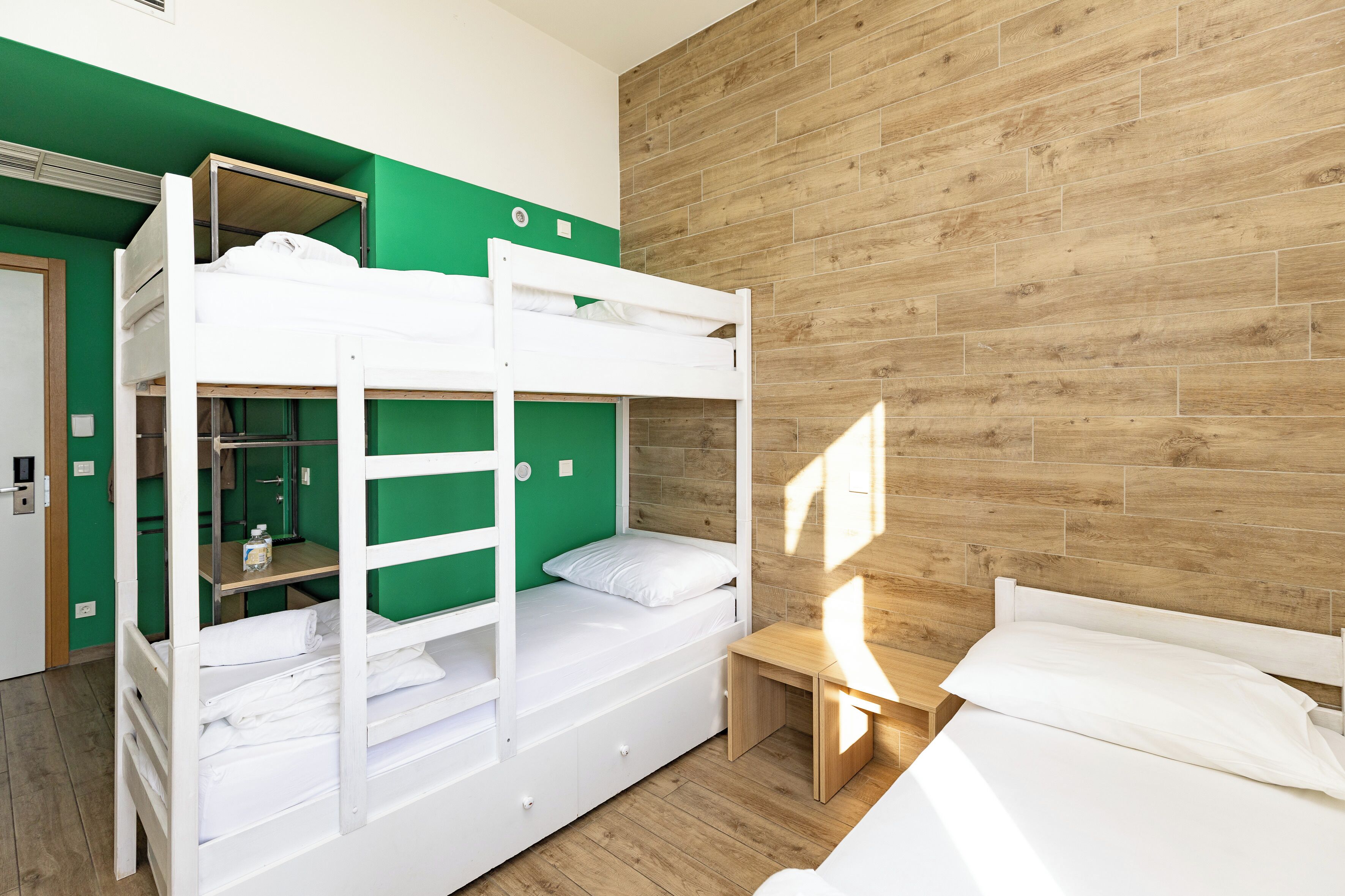 A bunk bed room with a wooden floor, green walls, and a wooden headboard.