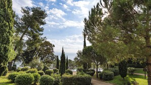 A landscaped garden with various trees and shrubs, a curved pathway, and a view of the sea in the background. - Hostel Link  (Lovran)
