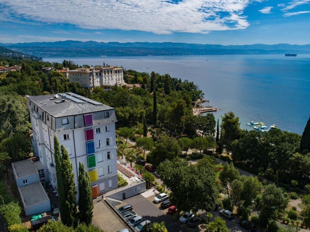 An aerial view of a coastal building complex with a parking area and a view of the sea.