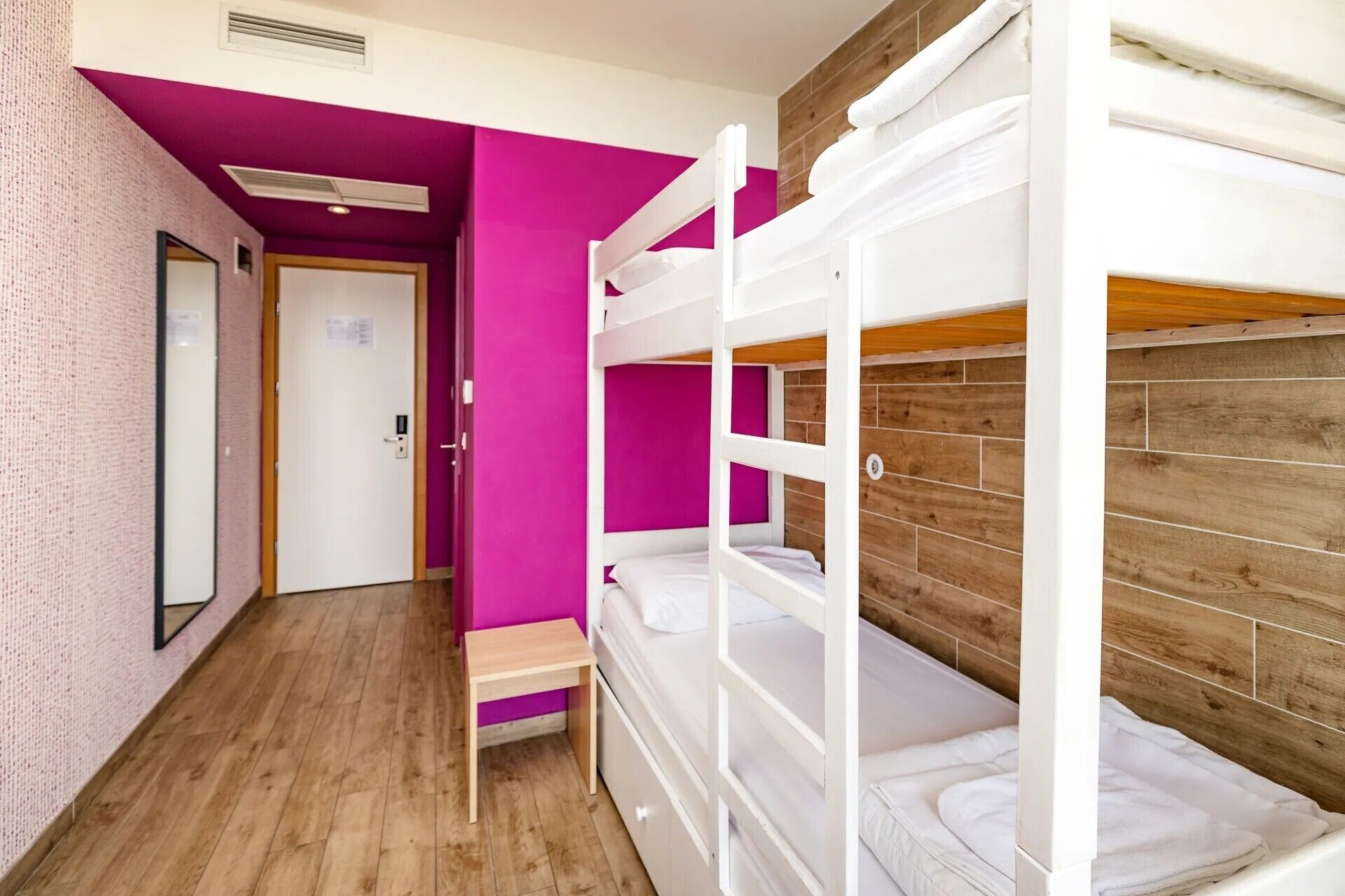 A room with bunk beds, wooden flooring, and a door with a handle.