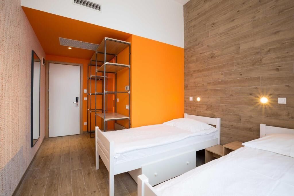 Una habitación con dos camas, una pared de madera y una estantería metálica.