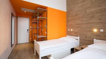 Una habitación con dos camas, una pared de madera y una estantería metálica.