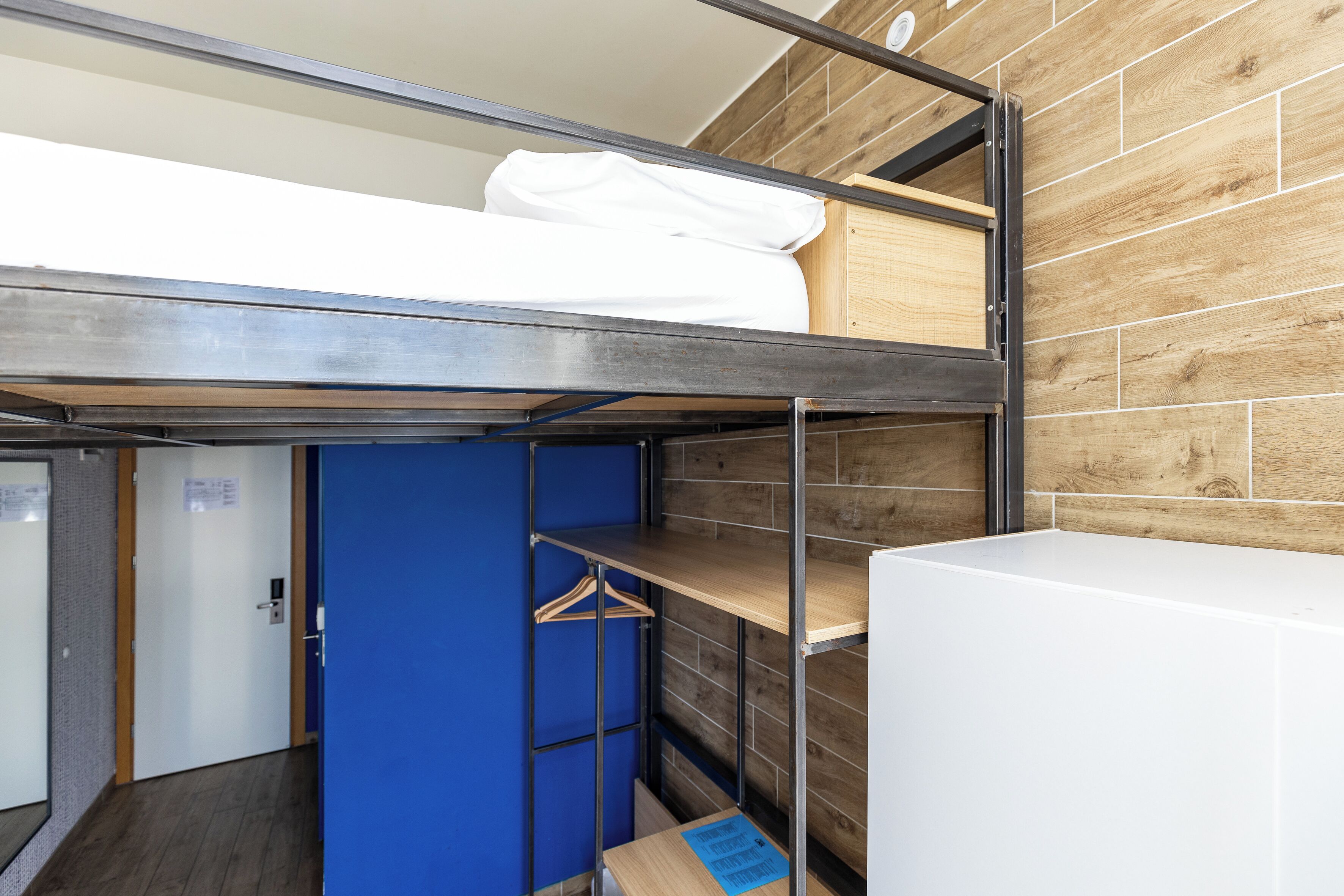 A bunk bed room with a wooden wall, a blue door, and a white wardrobe.