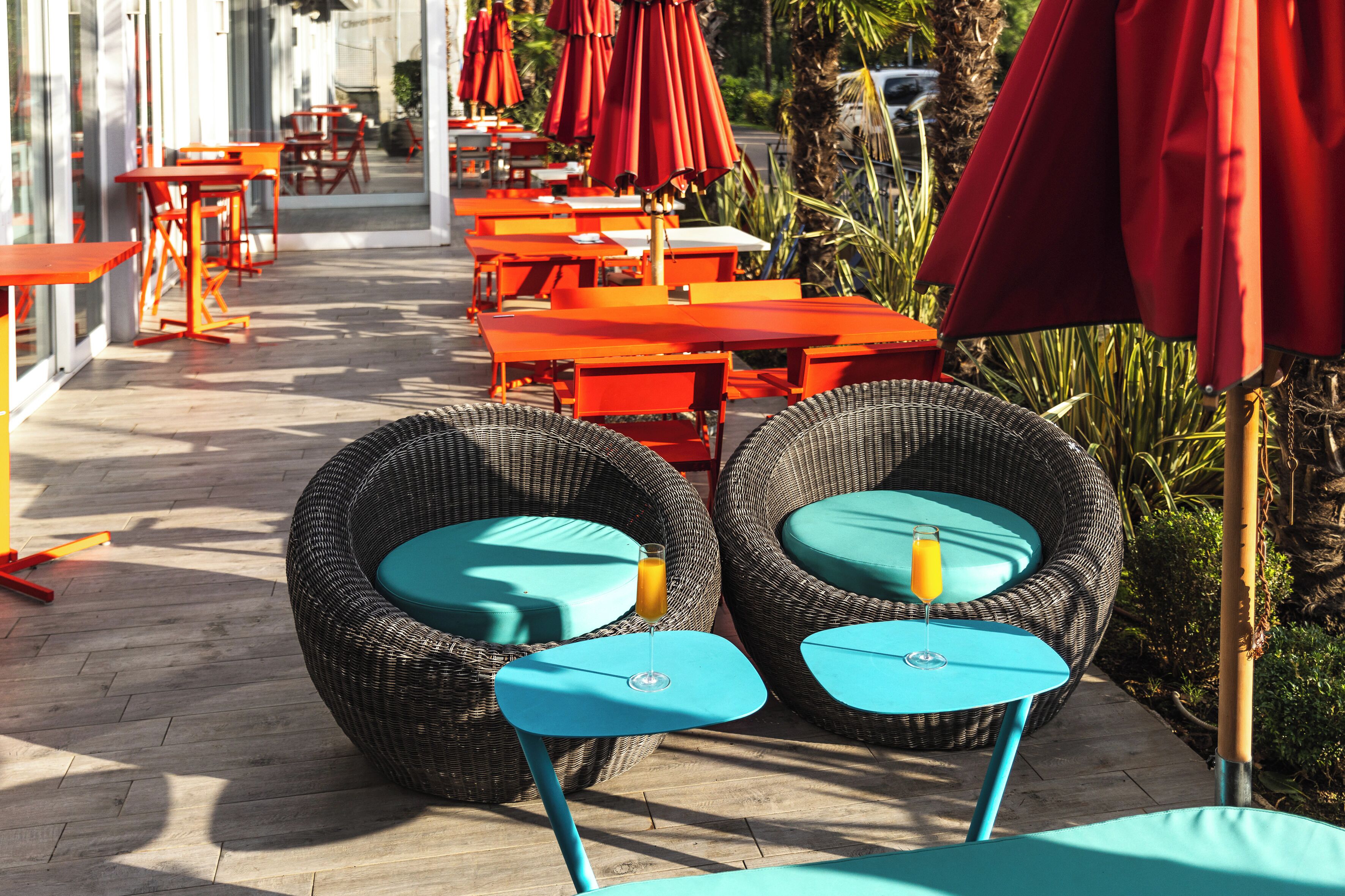 Outdoor seating with wicker chairs and tables, red umbrellas, and a pathway leading to a building.