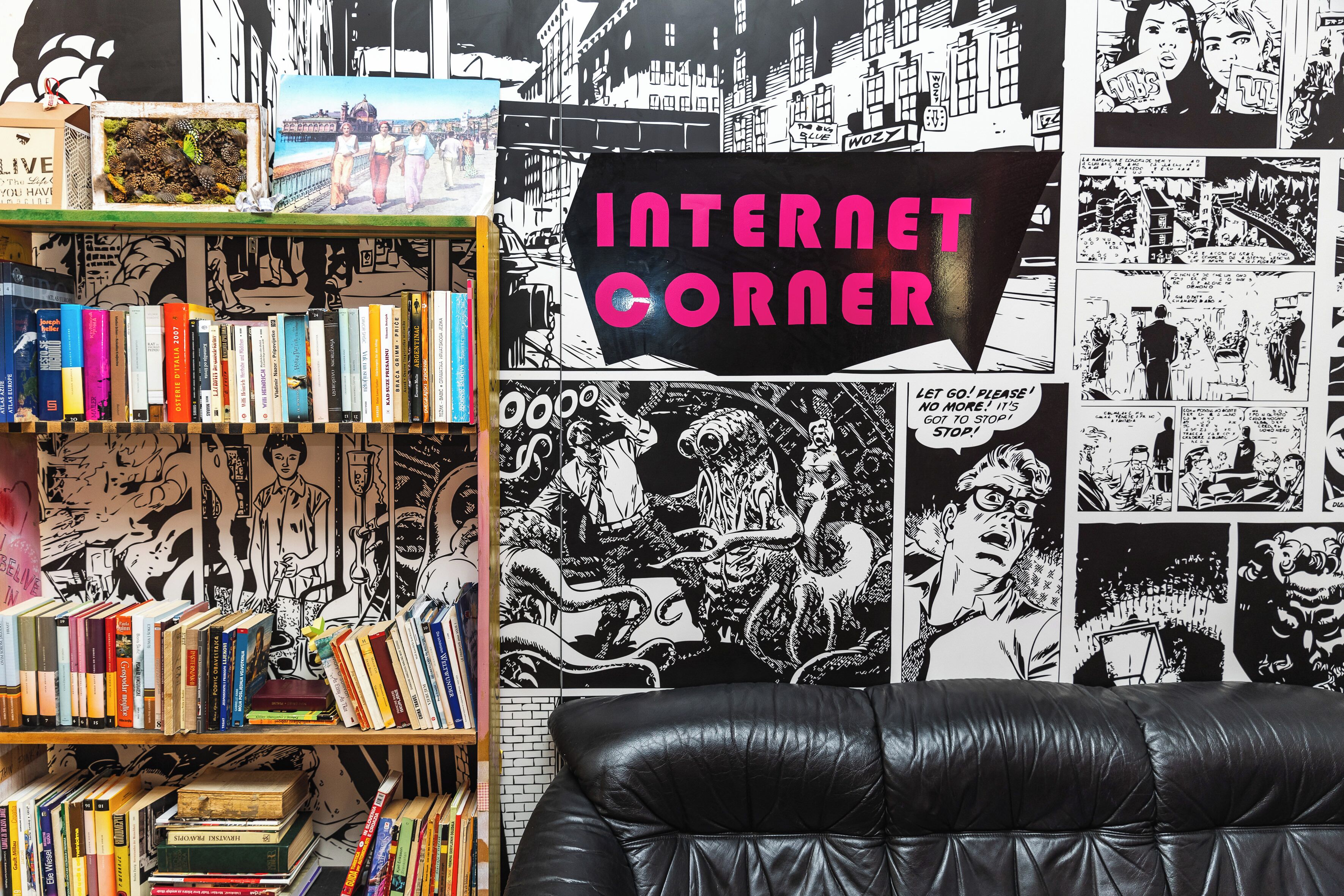 Una habitación con una estantería llena de libros, un sofá de cuero negro y una pared decorada con ilustraciones tipo cómic y el texto 
