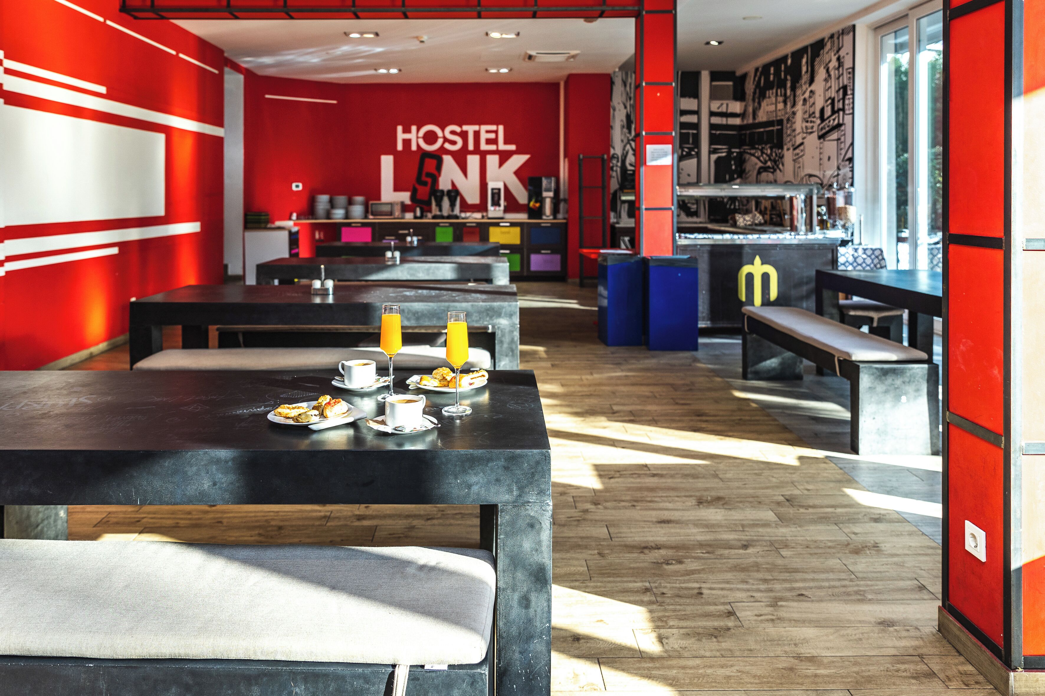 Een modern hostel interieur met een gemeenschappelijke eetruimte, banken en een open keuken.