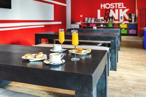 Comedor moderno de un hostal con mesas, alimentos para el desayuno y una pared roja con el nombre del hostal.