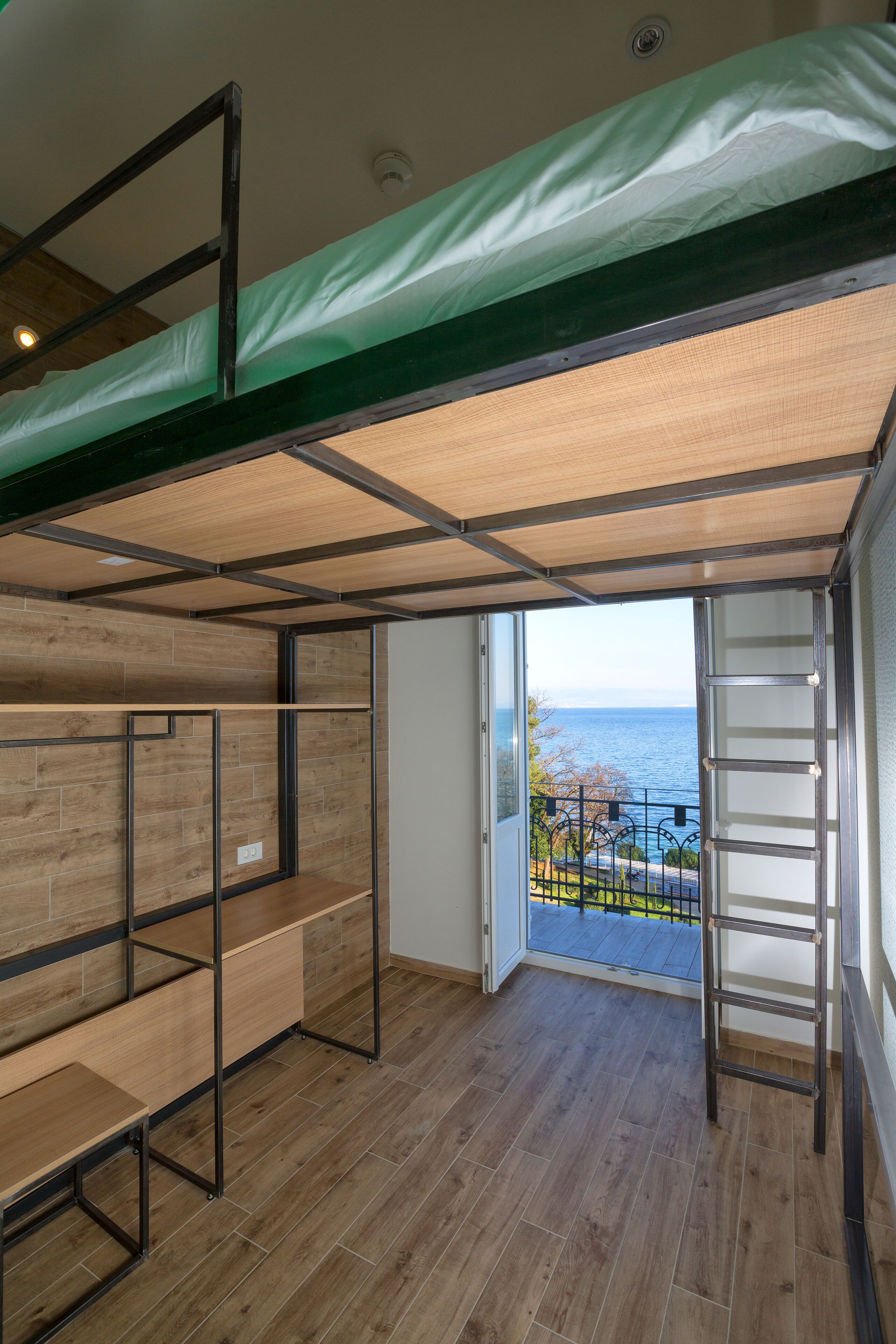 A room with a bunk bed, wooden flooring, and a balcony with a view of the sea.