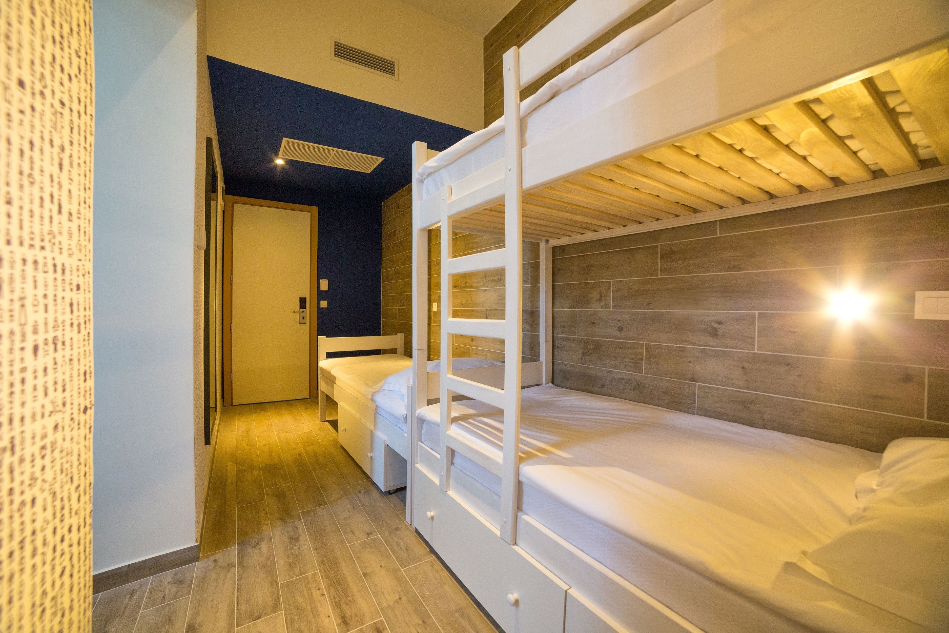 A hotel room with a bunk bed, a separate bed, and a wooden floor.