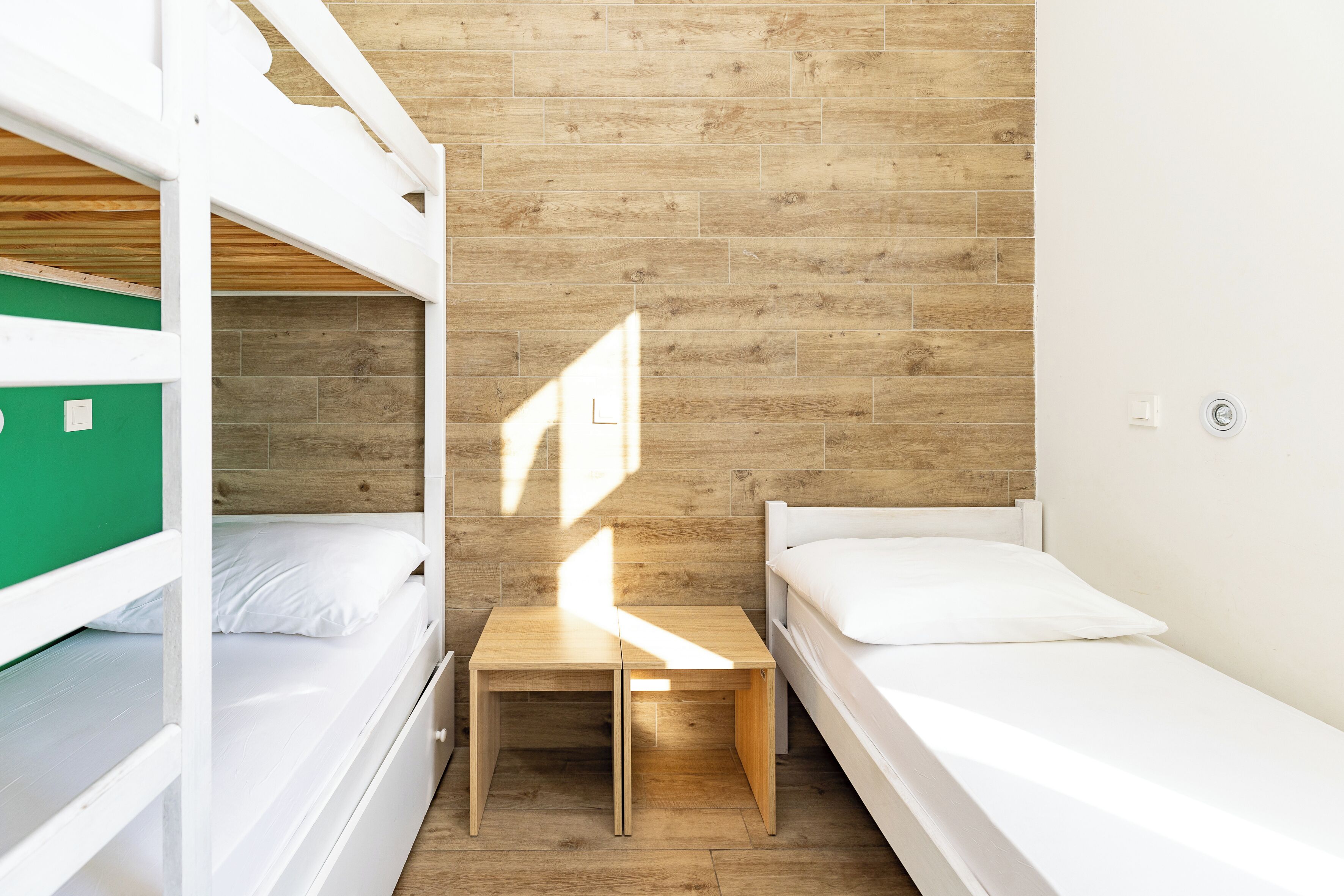 A dormitory room with bunk beds, a small wooden table, and a single bed.