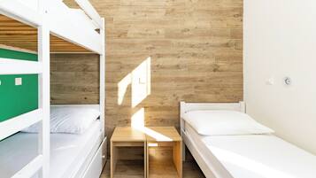 A dormitory room with bunk beds, a small wooden table, and a single bed.
