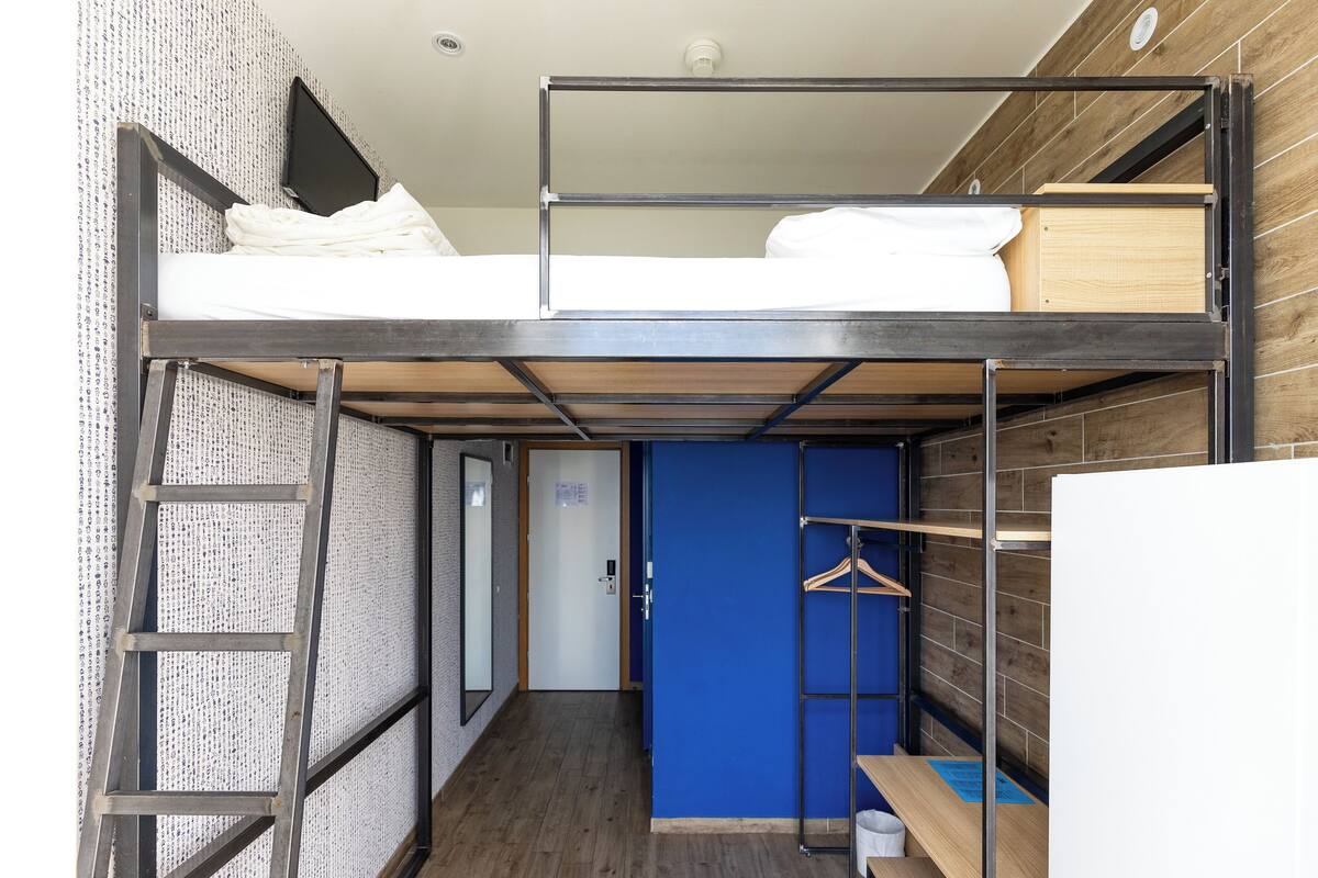A bunk bed room with a ladder, a blue wall, and a wooden floor.