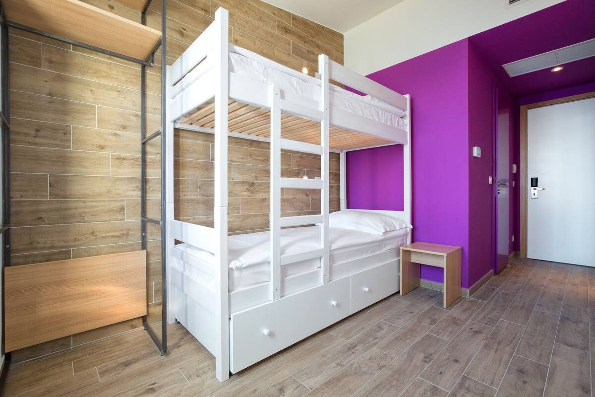 A bunk bed with storage drawers, a wooden wall, and a purple accent wall.