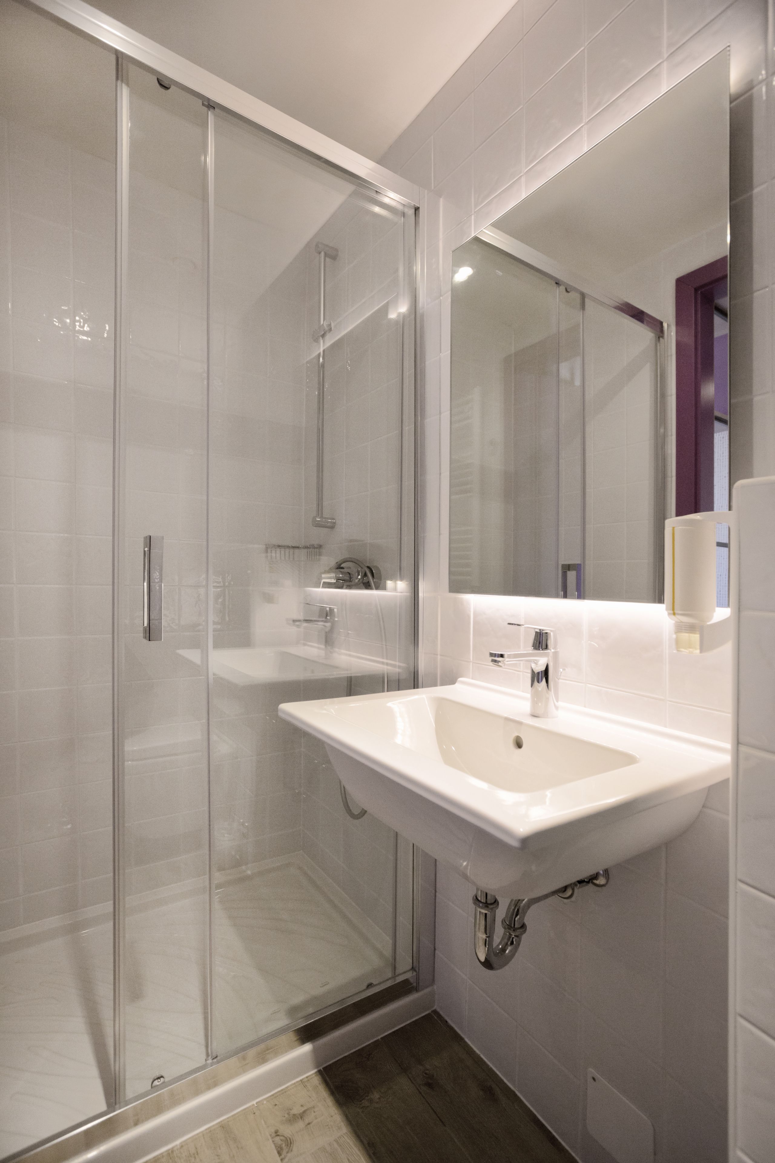 Une salle de bain moderne avec une douche à l’italienne en verre, un lavabo blanc et un grand miroir.