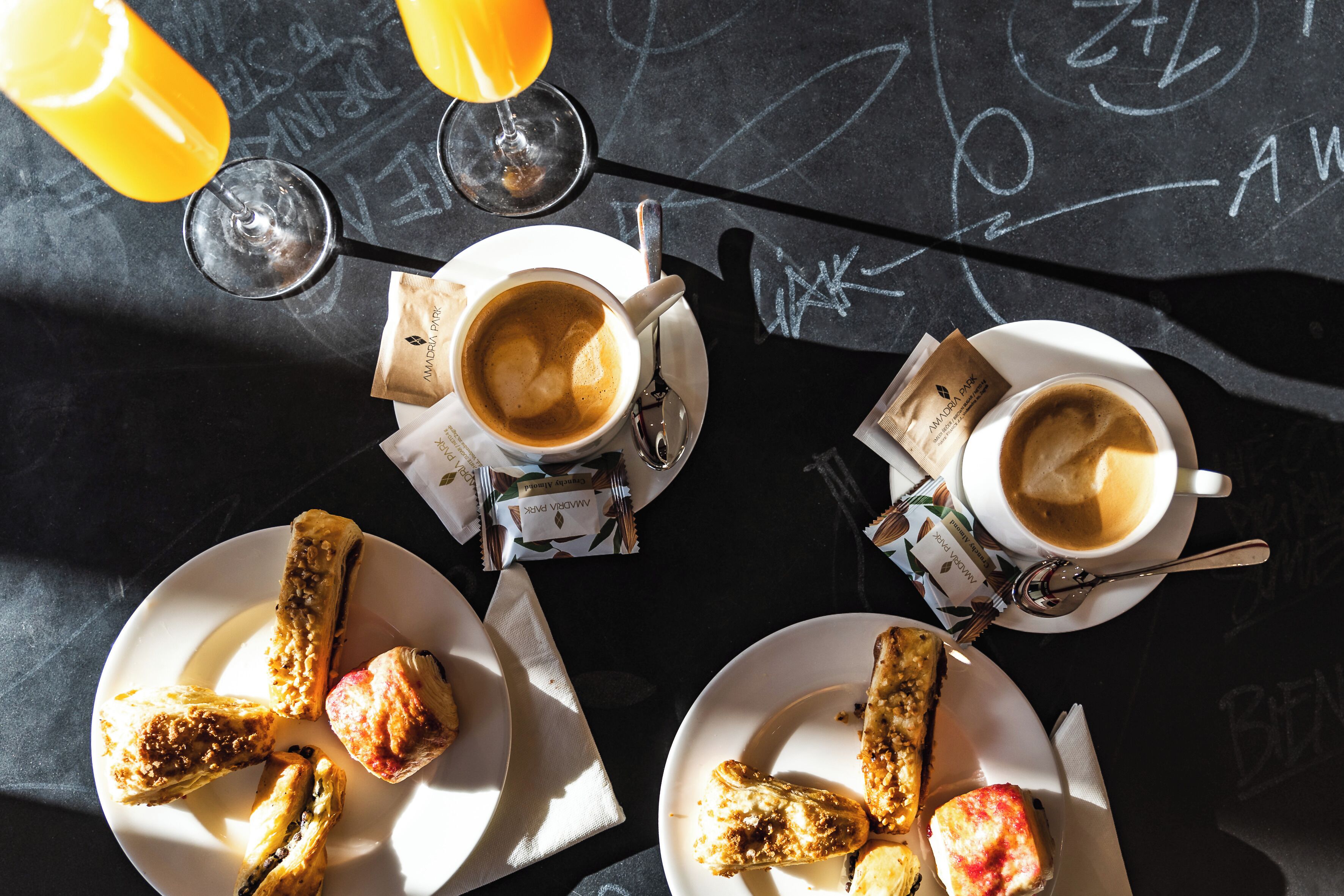 A table with two cups of coffee, two glasses of orange juice, and pastries.