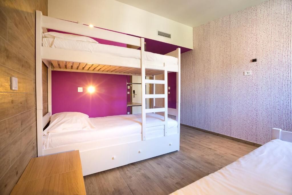 A bunk bed room with a wooden floor, a purple wall, and a white bed.