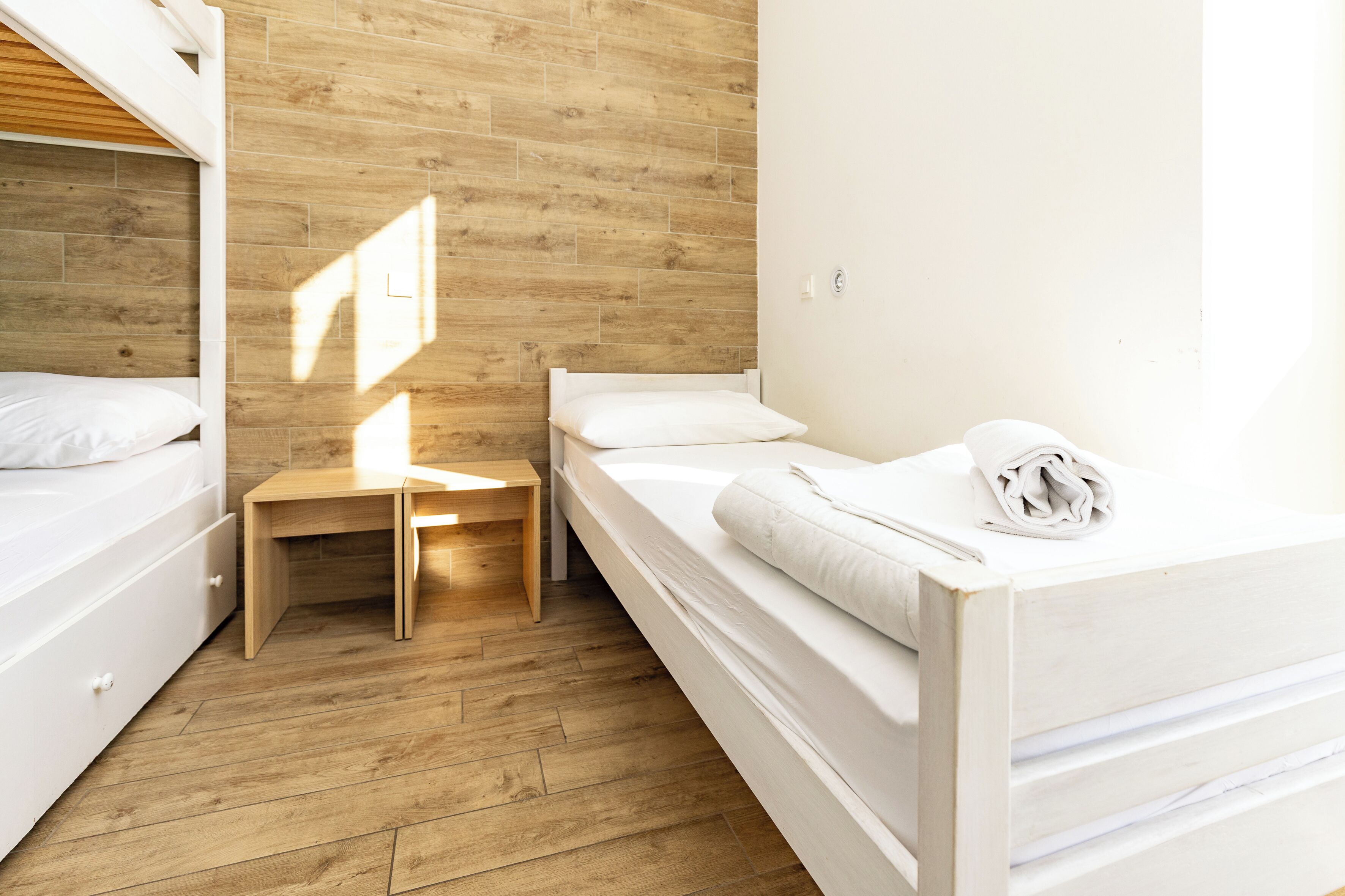 Un dormitorio con una cama doble, una cama individual, piso de madera y una pequeña mesa de madera.