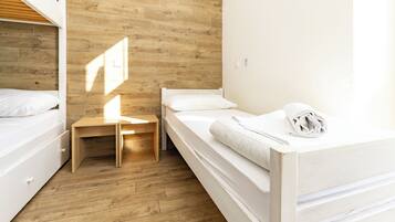 Un dormitorio con una cama doble, una cama individual, piso de madera y una pequeña mesa de madera.