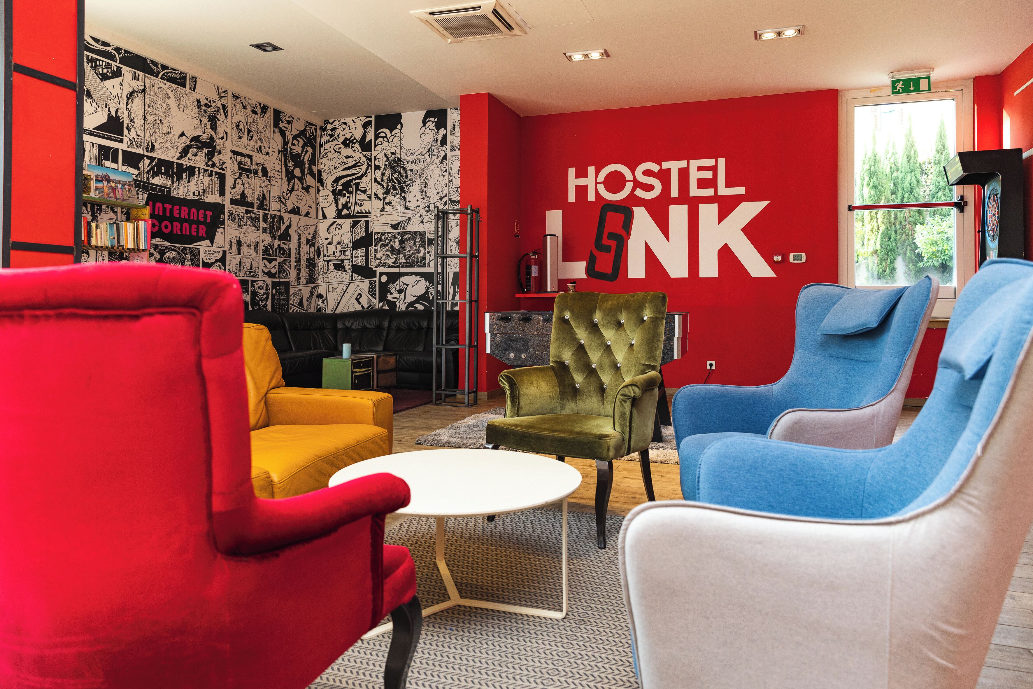 A modern hostel interior with vibrant red walls, a comic strip mural, and colorful seating.