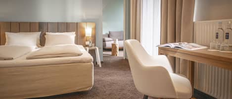 A hotel room with a large bed, a desk with a chair, a lamp, and a TV mounted on the wall.
