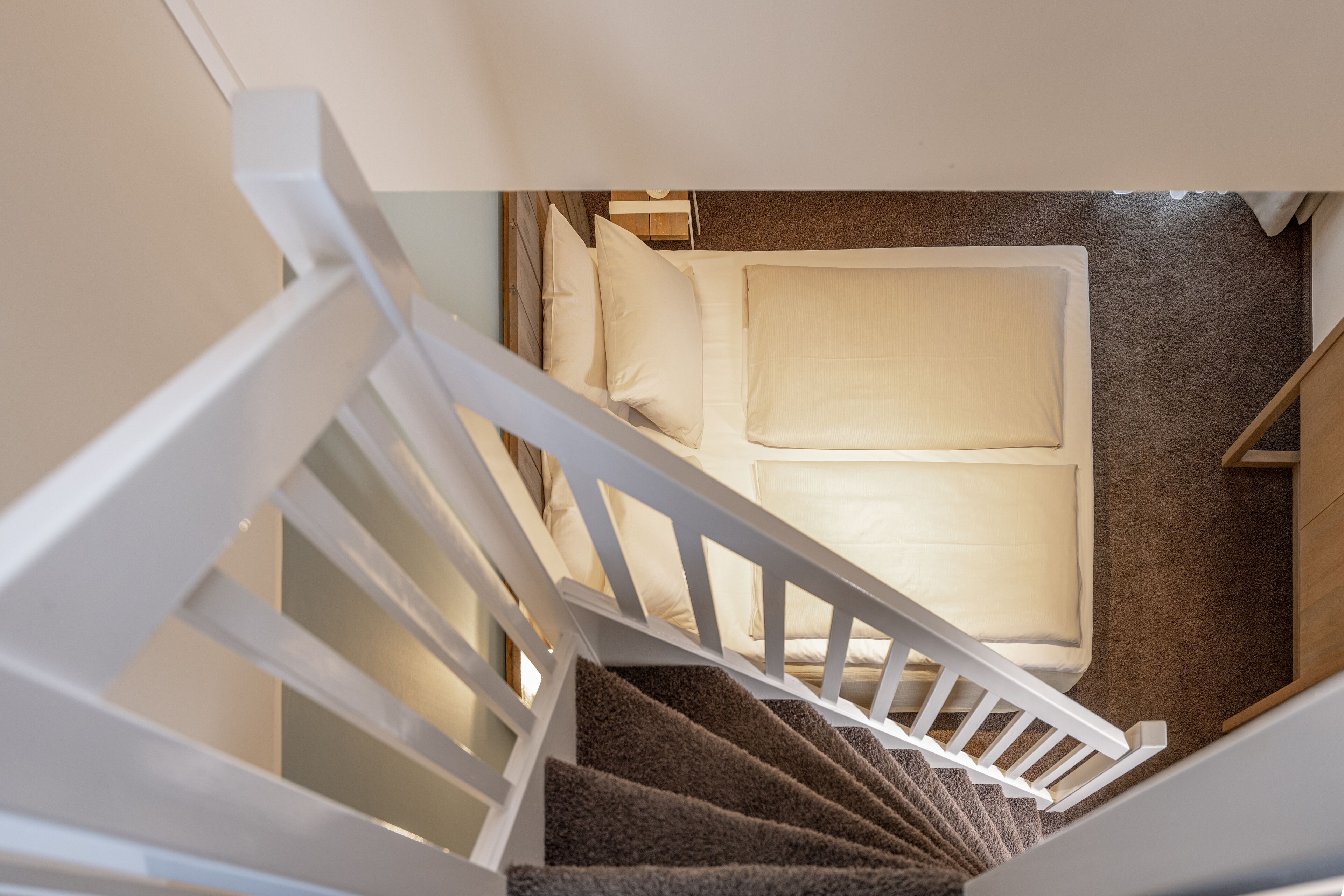 A staircase leading to a bedroom with a bed, pillows, and a carpeted floor.