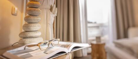 A neatly arranged hotel room with a lamp on a bedside table, an open book, and a pair of glasses.