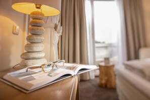 A neatly arranged hotel room with a lamp on a bedside table, an open book, and a pair of glasses.