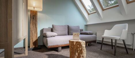 A modern loft bedroom with a sloped ceiling, a sofa, a chair, a lamp, and a sign on a wooden stump.