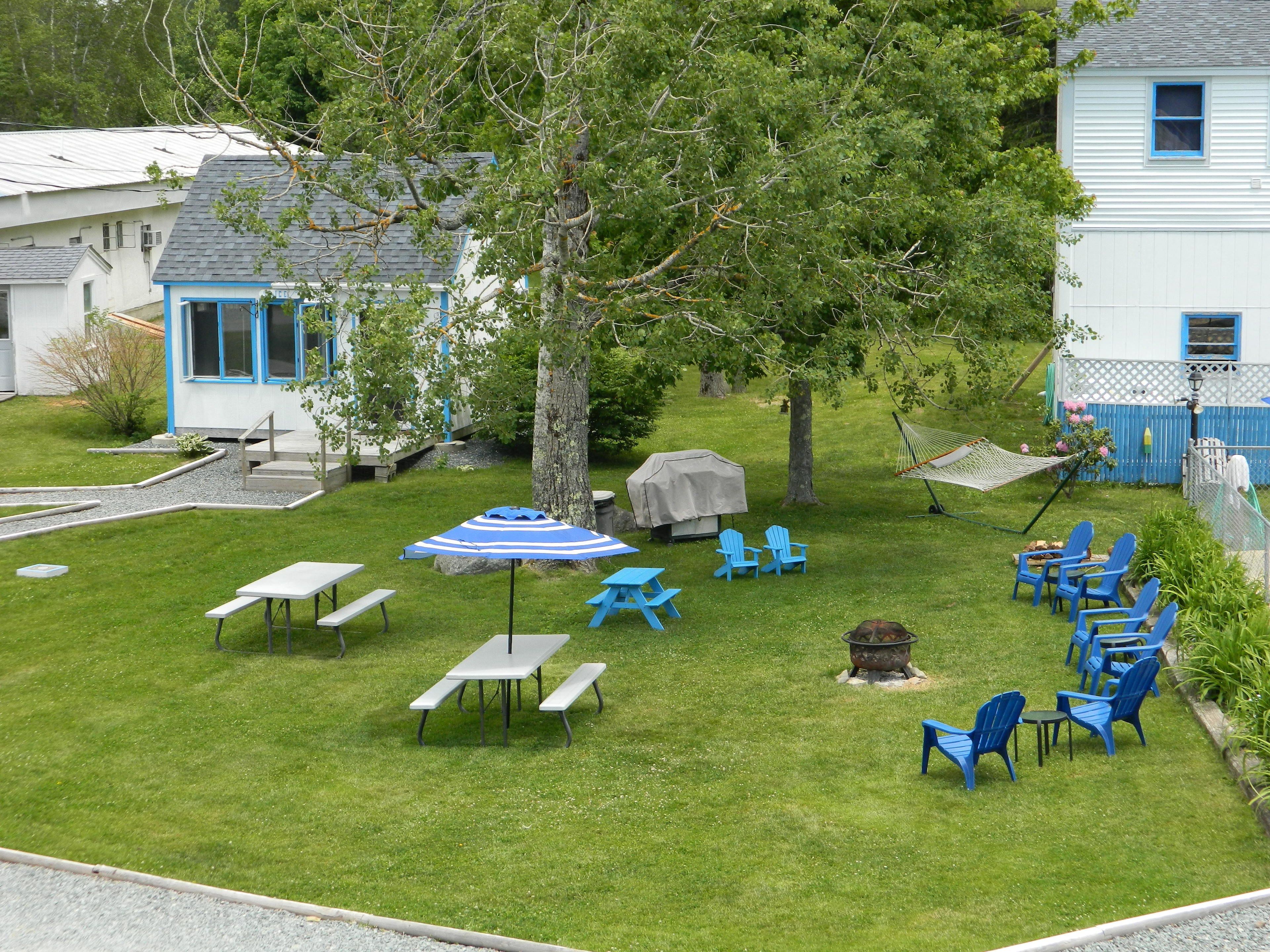 A backyard with picnic tables, blue chairs, and a barbecue grill.