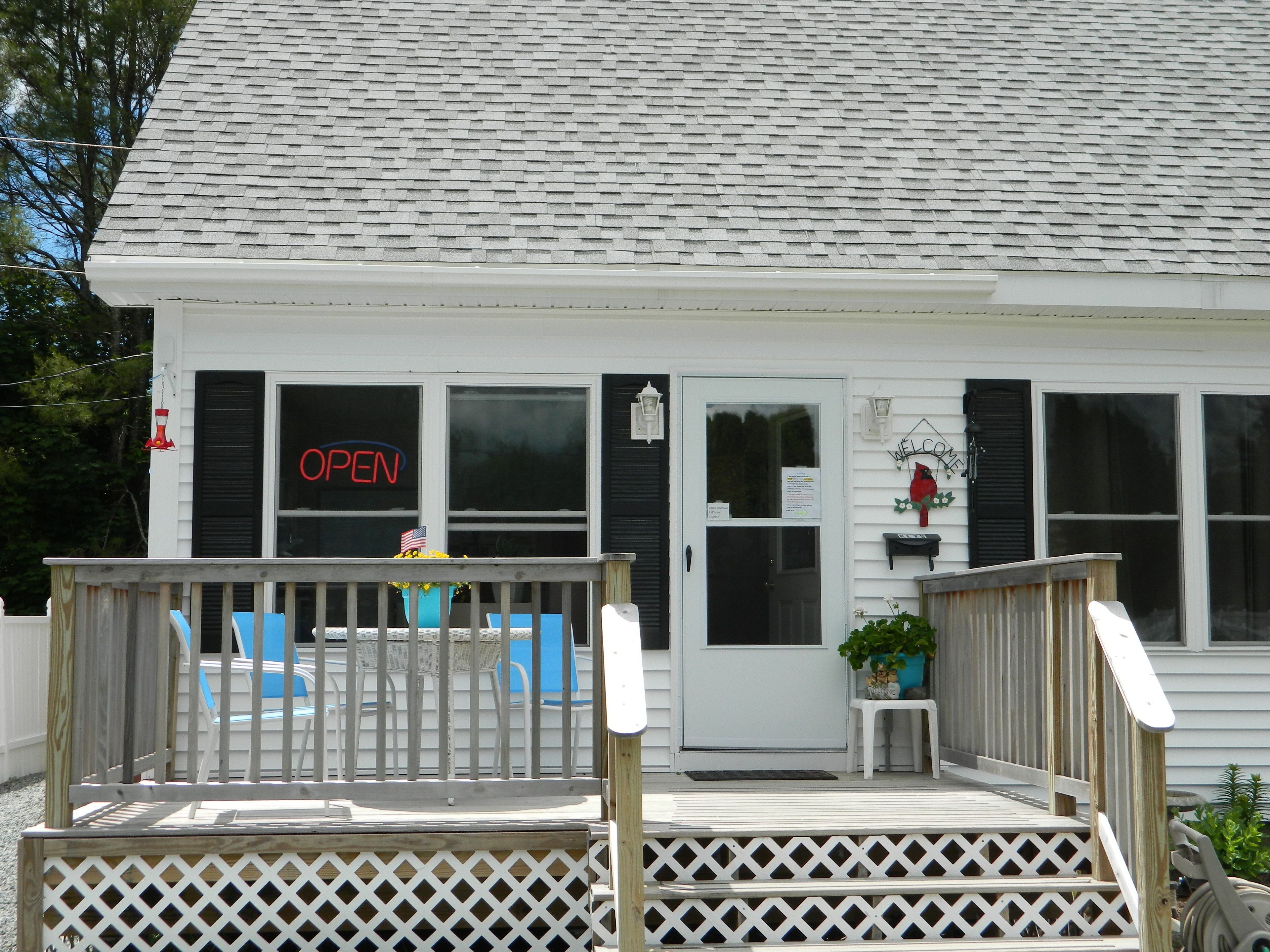 A white building with a porch, a 'OPEN' sign, and outdoor seating.