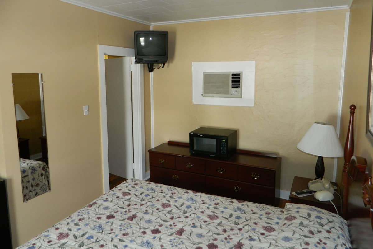 A hotel room with a bed, a dresser, a television, a microwave, a lamp, and a mirror.