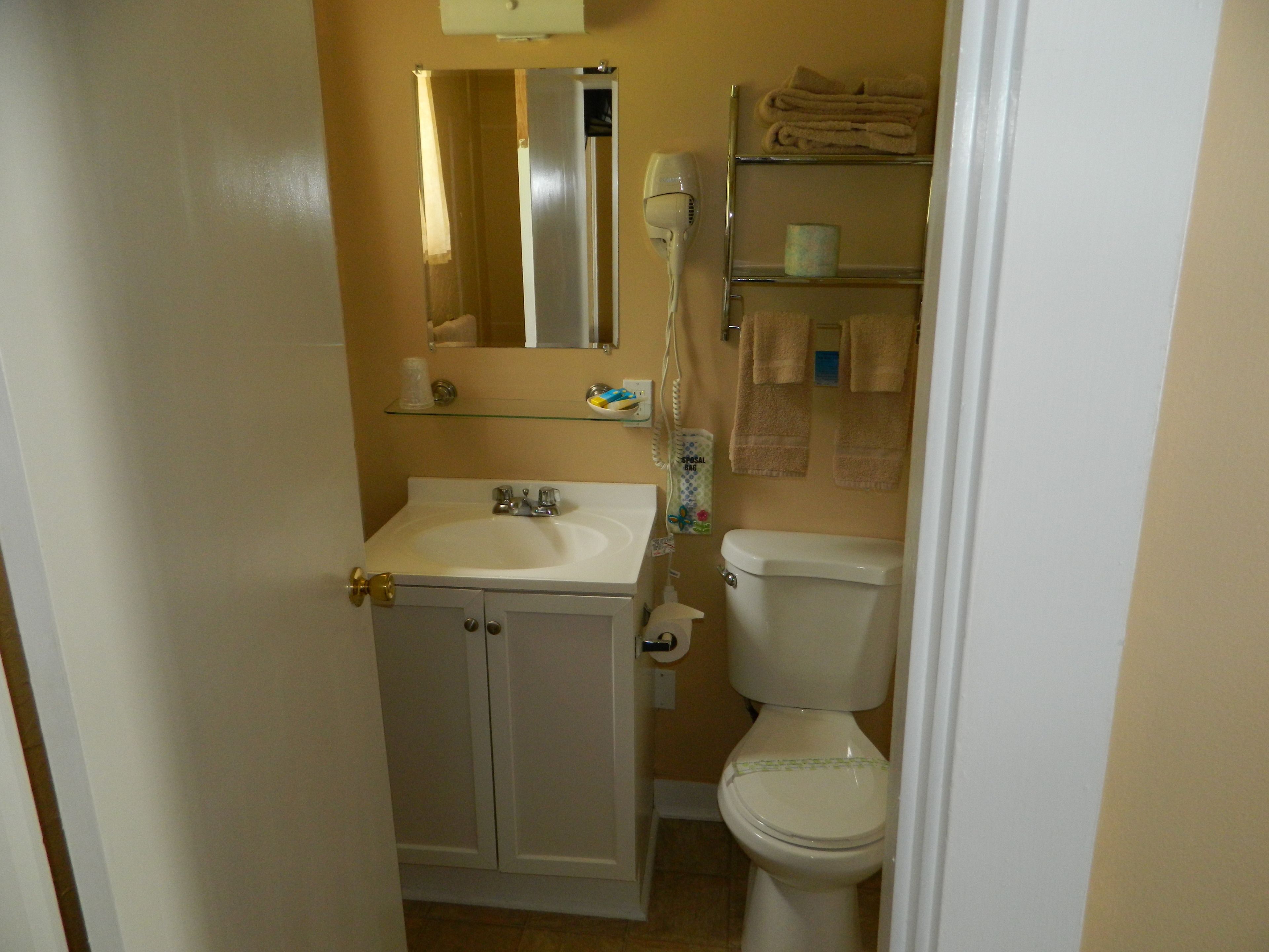 A small bathroom with a white sink, a mirror, a toilet, and a shelf with towels.