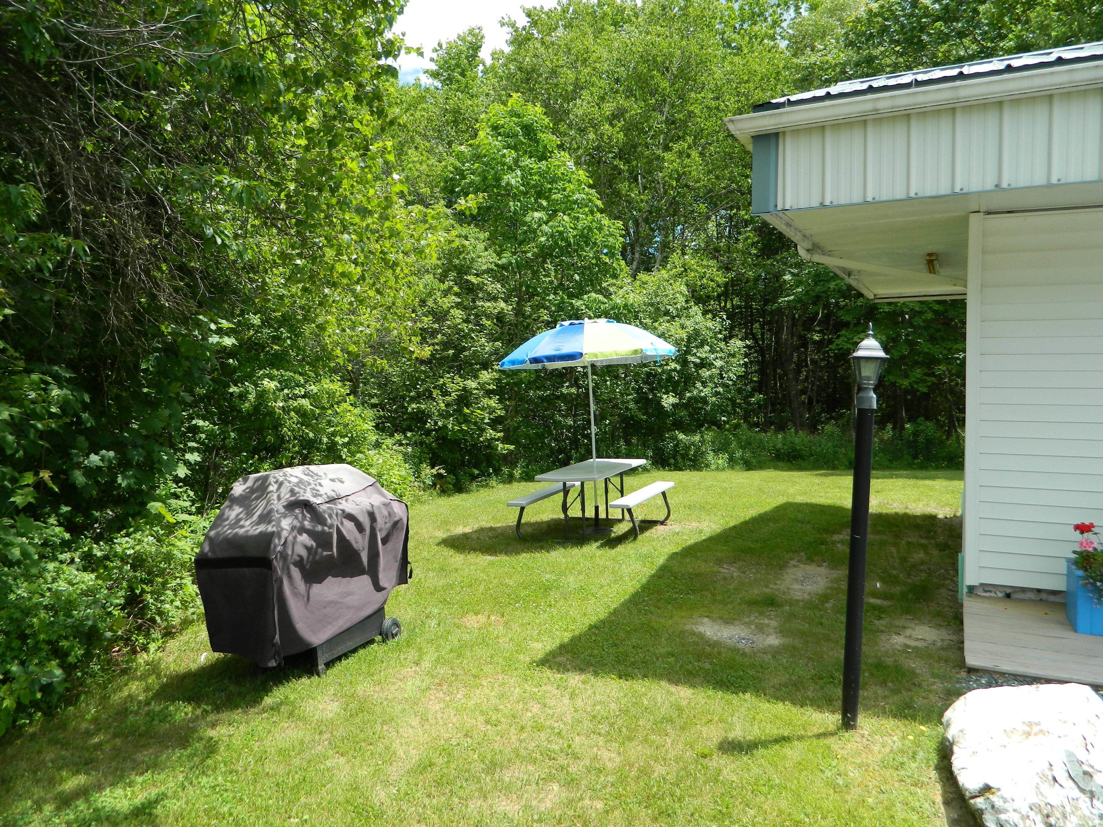 En have med grill under tag, et picnicbord og en parasol.