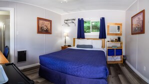 A bedroom with a large bed, a window with curtains, a bedside table with a lamp, and a wall-mounted air conditioner.