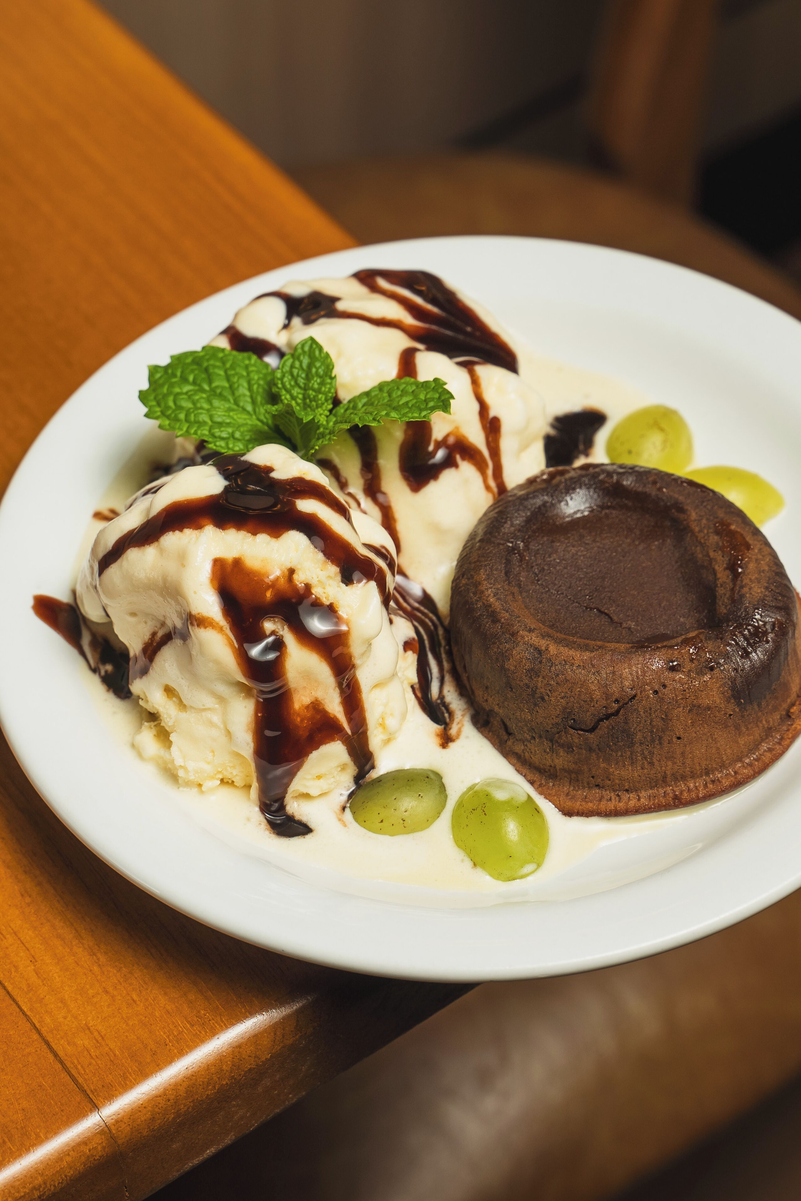 A dessert plate with ice cream and chocolate cake, garnished with mint leaves and grapes.