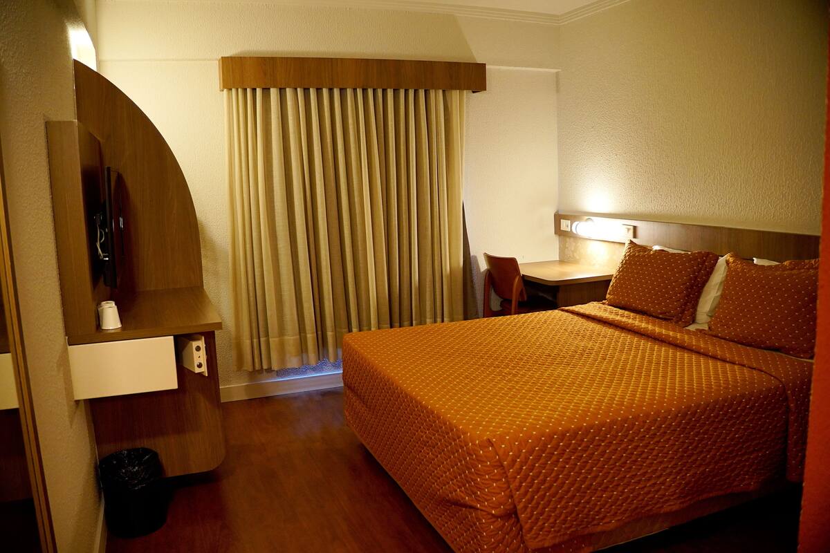 A hotel room with a bed, a desk, a chair, a TV, and a curtain.