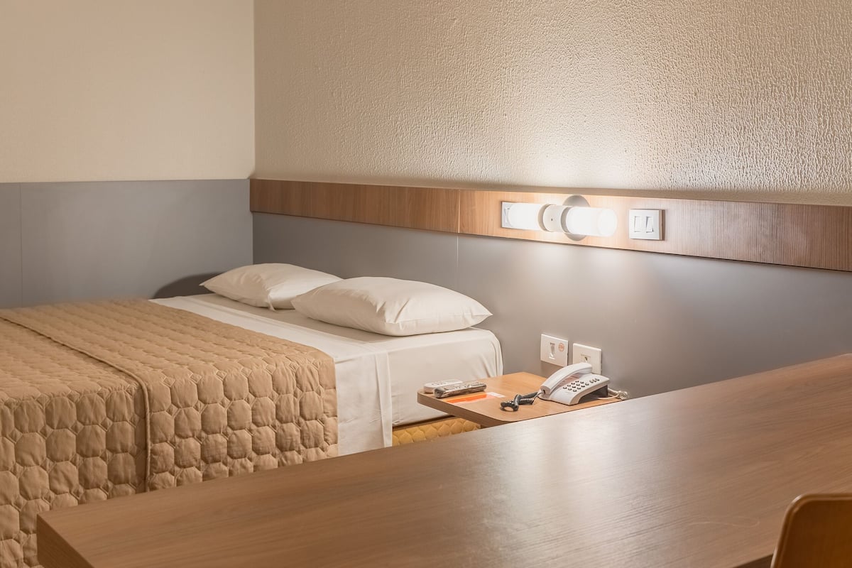A hotel room with a bed, bedside table, and a desk with a chair.