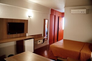 Una habitación compacta con televisión de pantalla plana, una kitchenette pequeña, una cama con cubrecama acolchado y un armario.