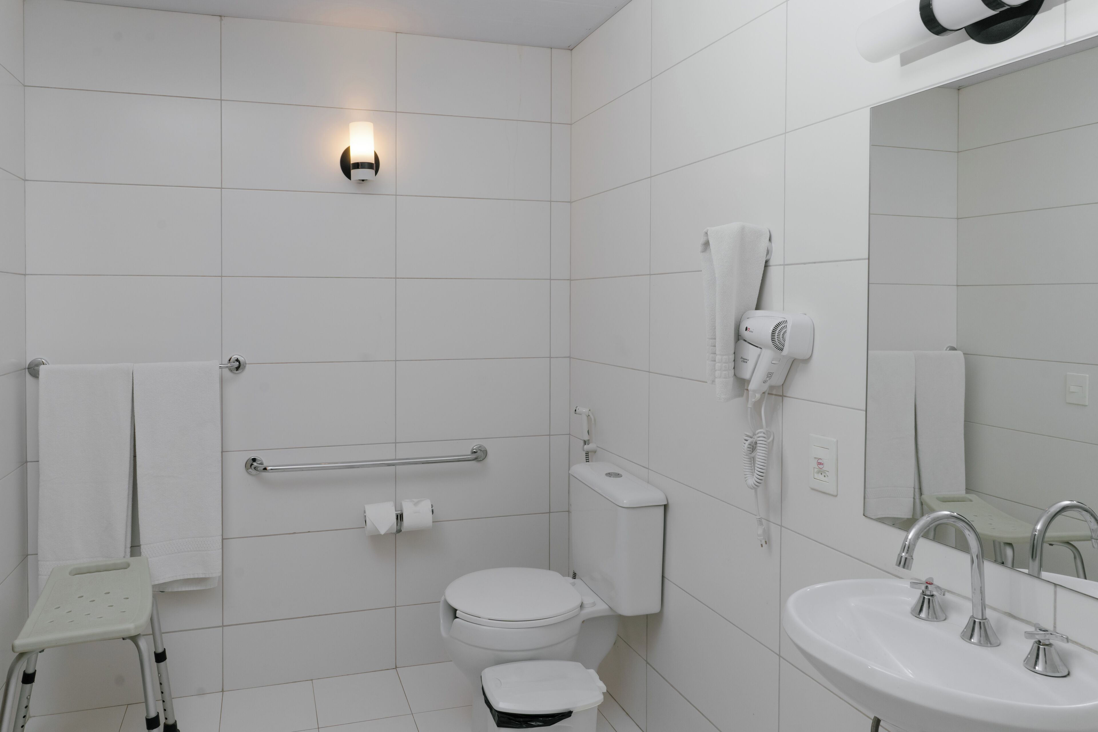 A modern bathroom with a white toilet, a sink with two faucets, a hand dryer, and a towel rack.